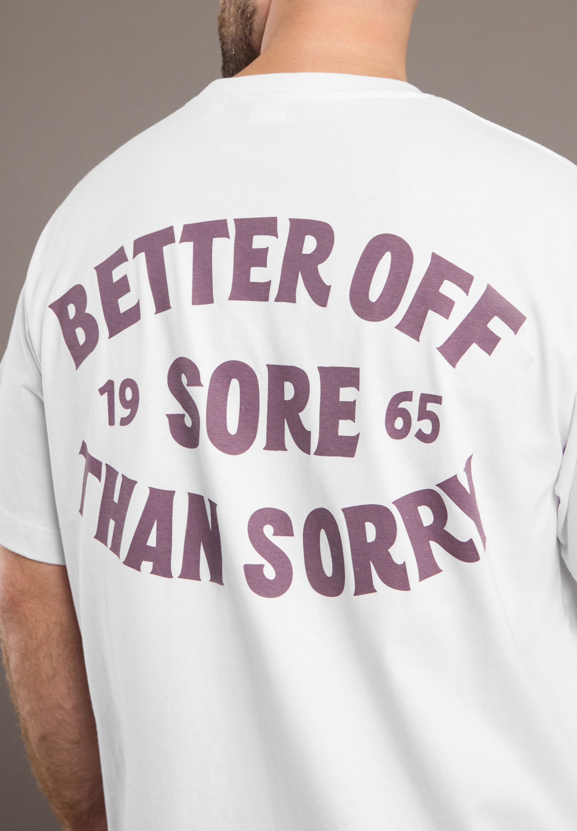 White t-shirt with purple text 'Better Off Sore Than Sorry' on the back, worn by a person.