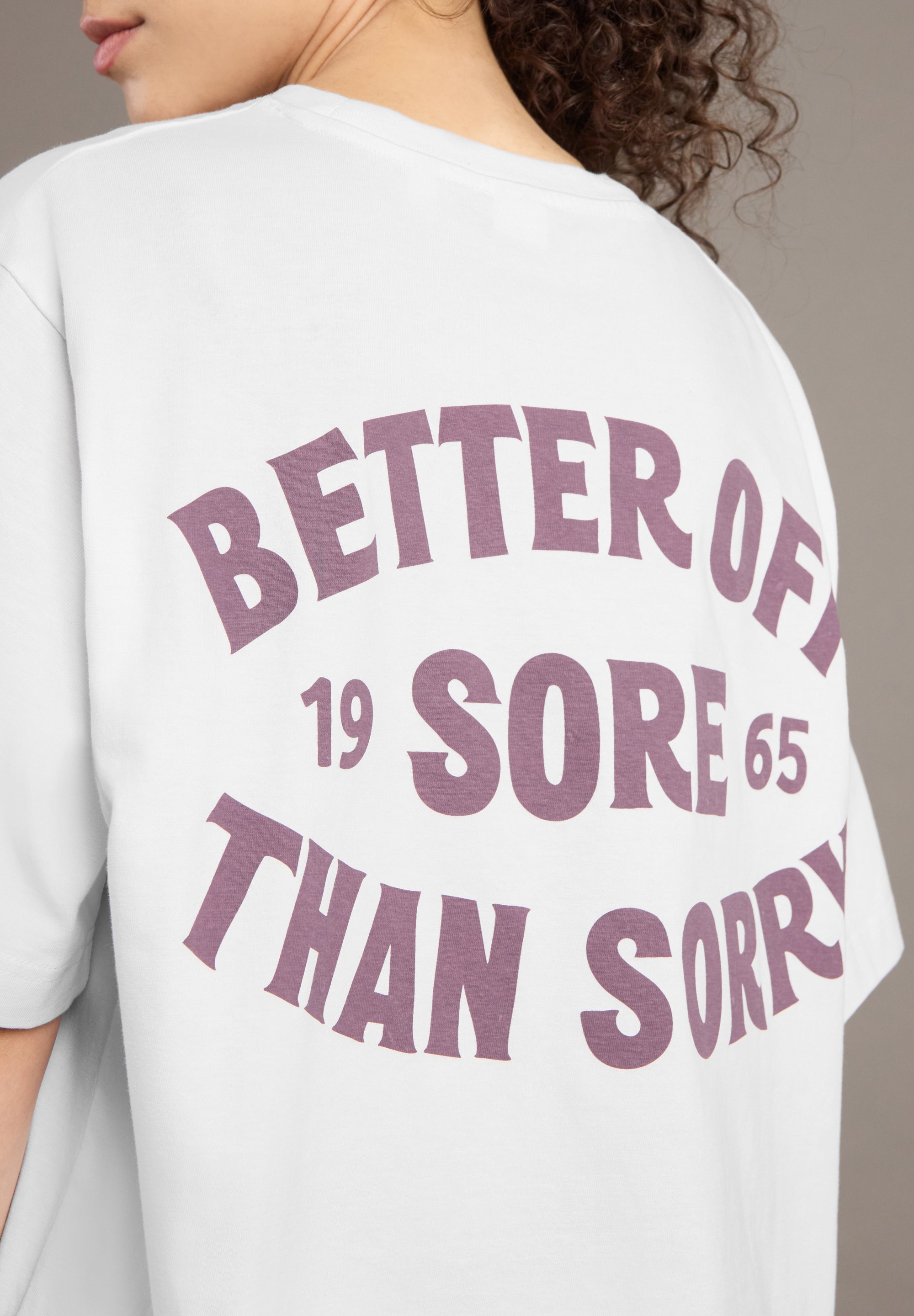 White t-shirt with purple text on the back, worn by a person.