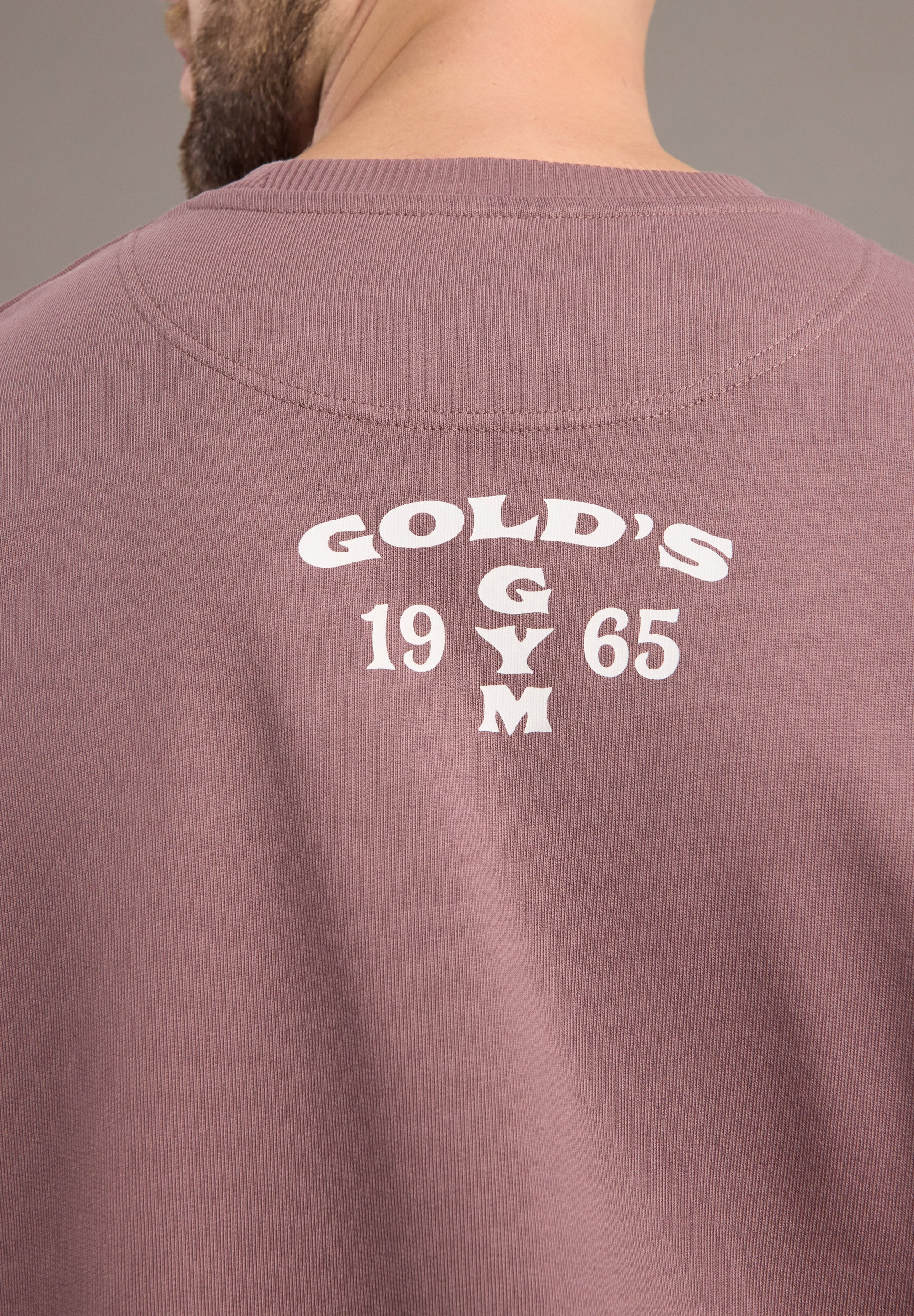 Back of a maroon sweatshirt with 'Gold's Gym 1965' text on a neutral background