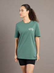 Woman wearing a green t-shirt with a logo on a brown background