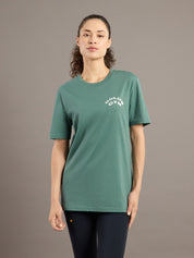Person wearing a green t-shirt with a logo on a brown background