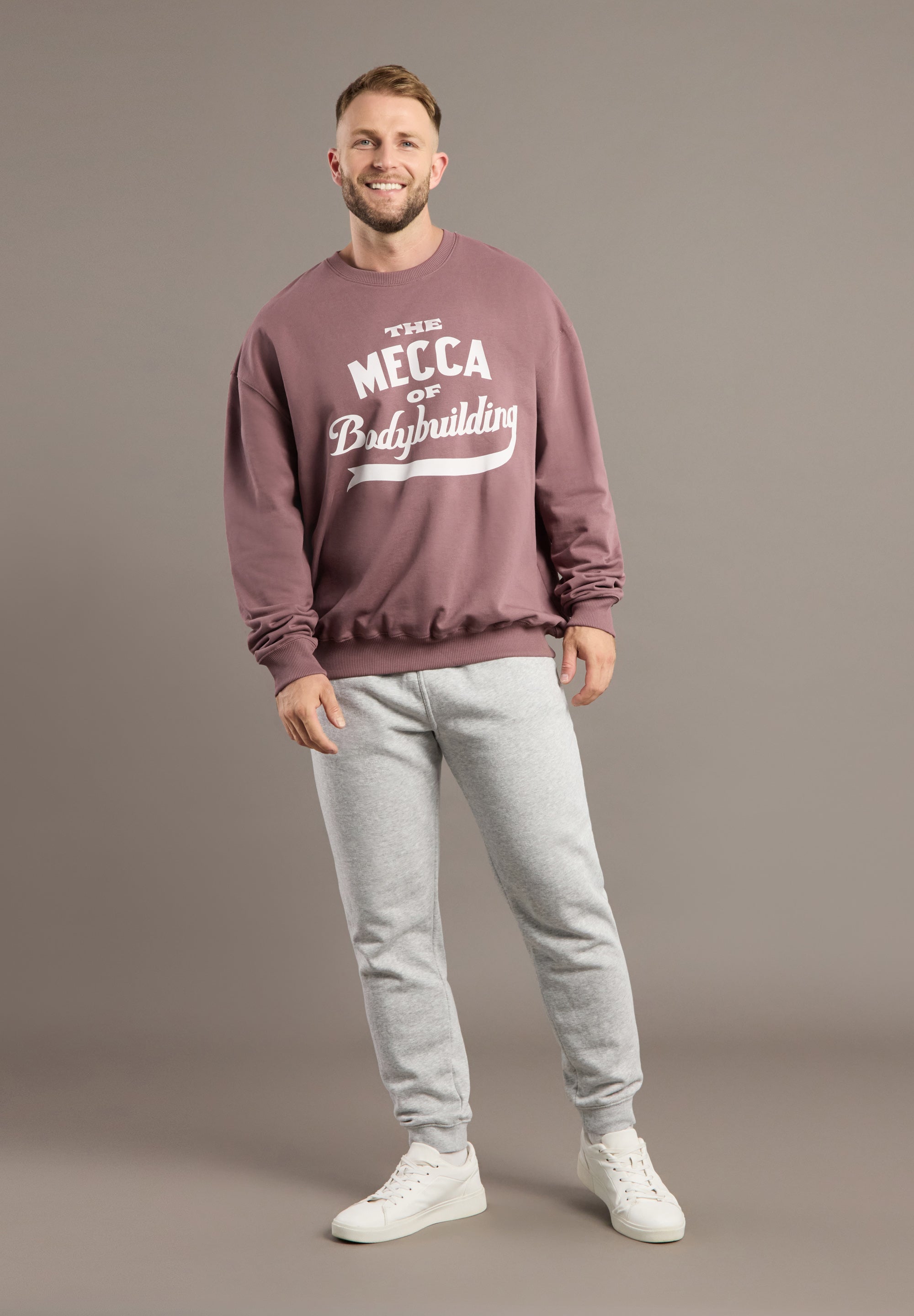 Man wearing a maroon sweatshirt with text and gray pants on a brown background