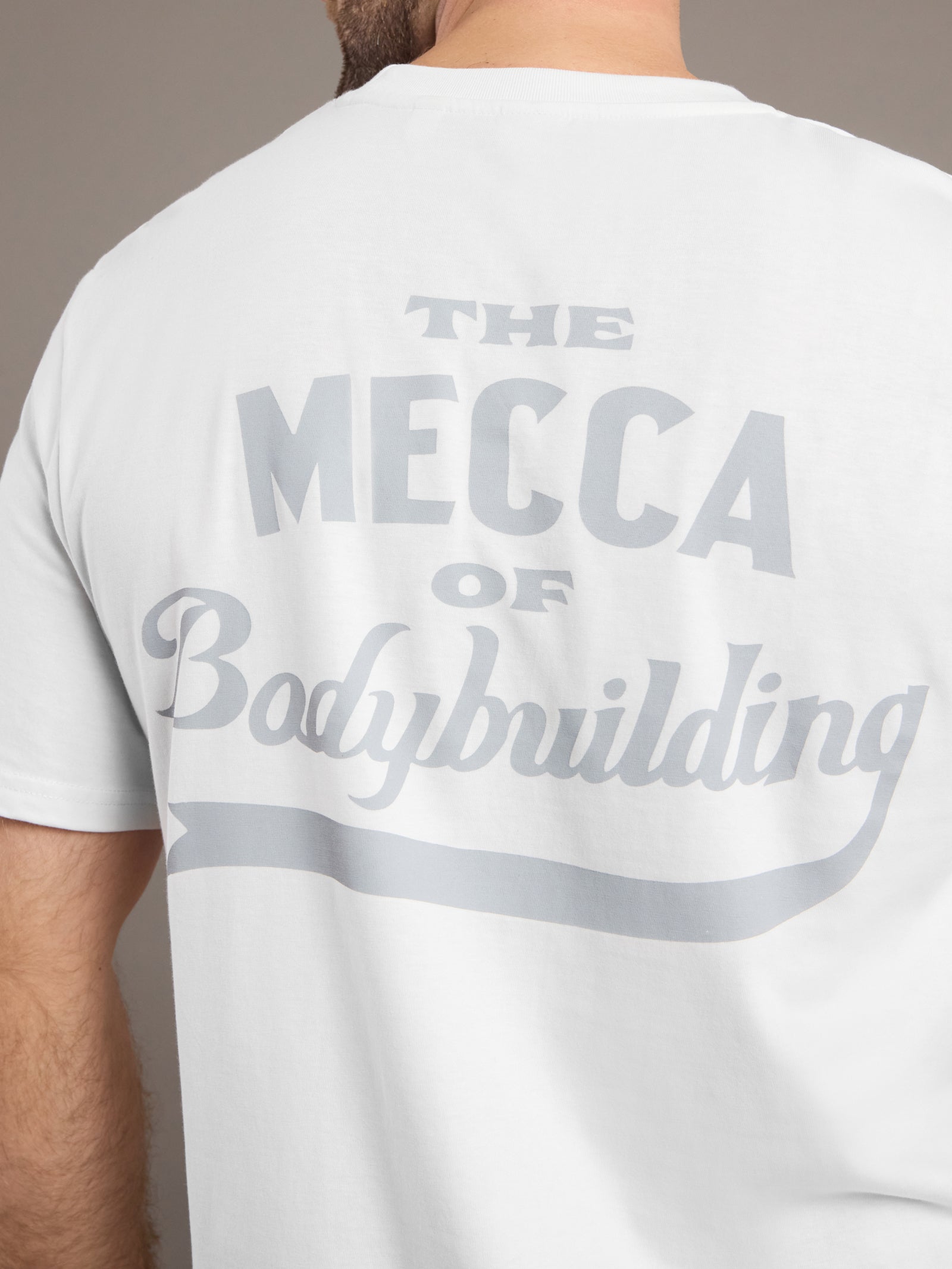 White t-shirt with 'The Mecca of Bodybuilding' text on the back, worn by a person.