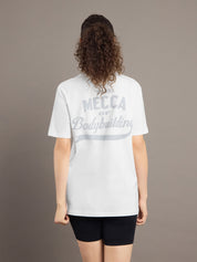 Person wearing a white t-shirt with 'Mecca of Bodybuilding' text on the back against a brown background