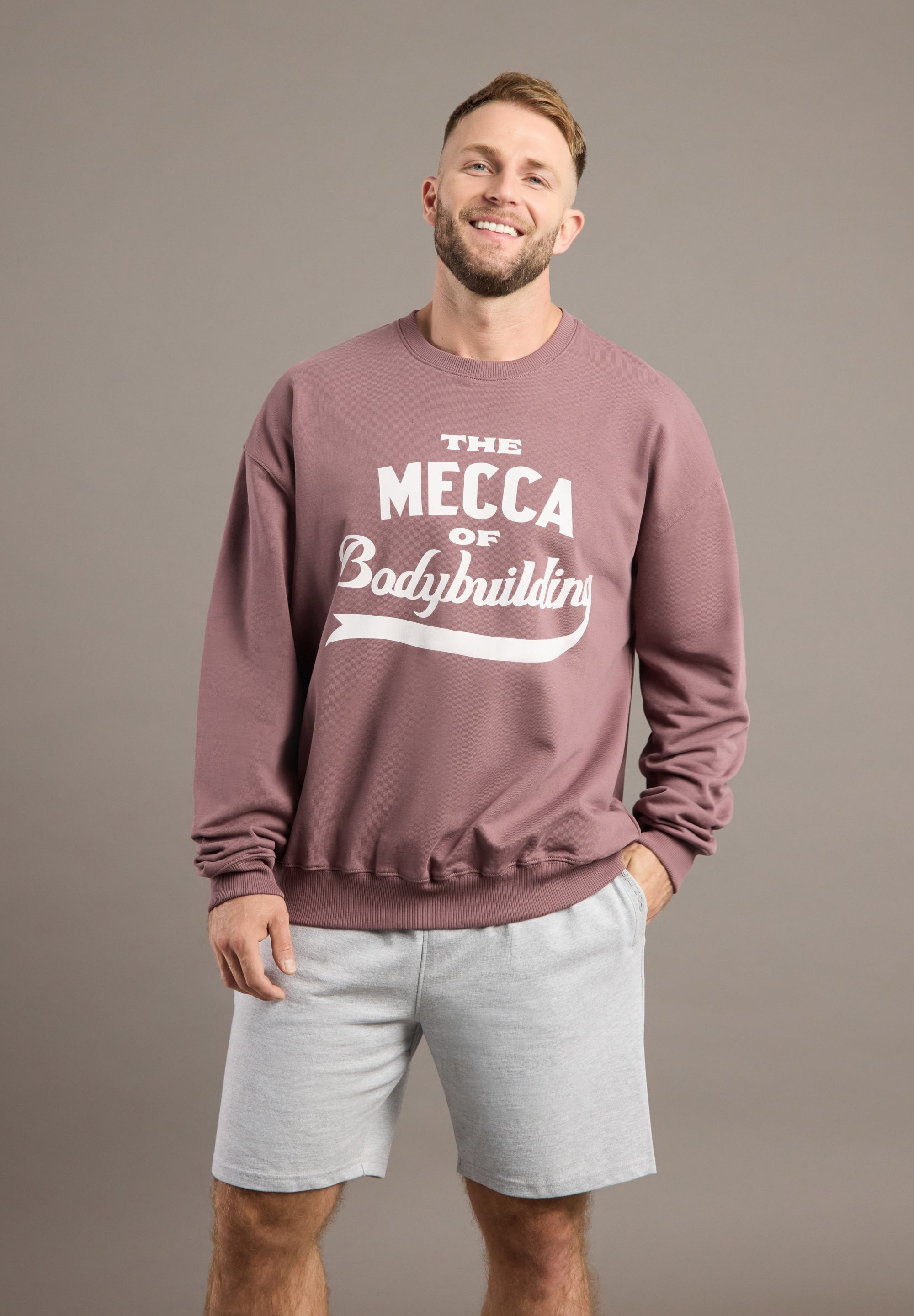 Man wearing a maroon sweatshirt with 'The Mecca of Bodybuilding' text on a gray background