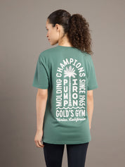 Person wearing a green t-shirt with text on the back, standing against a brown background