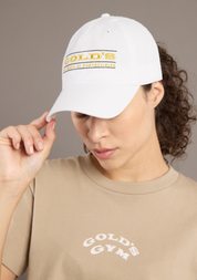 Person wearing a white cap with 'Gold's' branding and a beige t-shirt with 'Gold's Gym' branding against a neutral background.