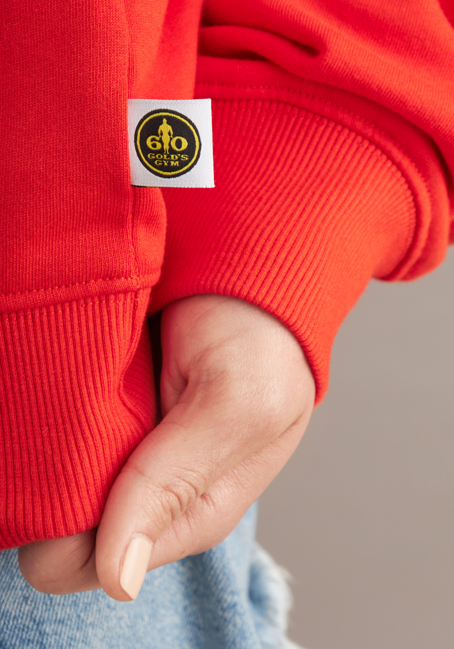 Close-up of a red sweatshirt with a brand logo on the sleeve against a neutral background