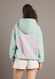Person wearing a light green hoodie with pink text on the back against a plain background
