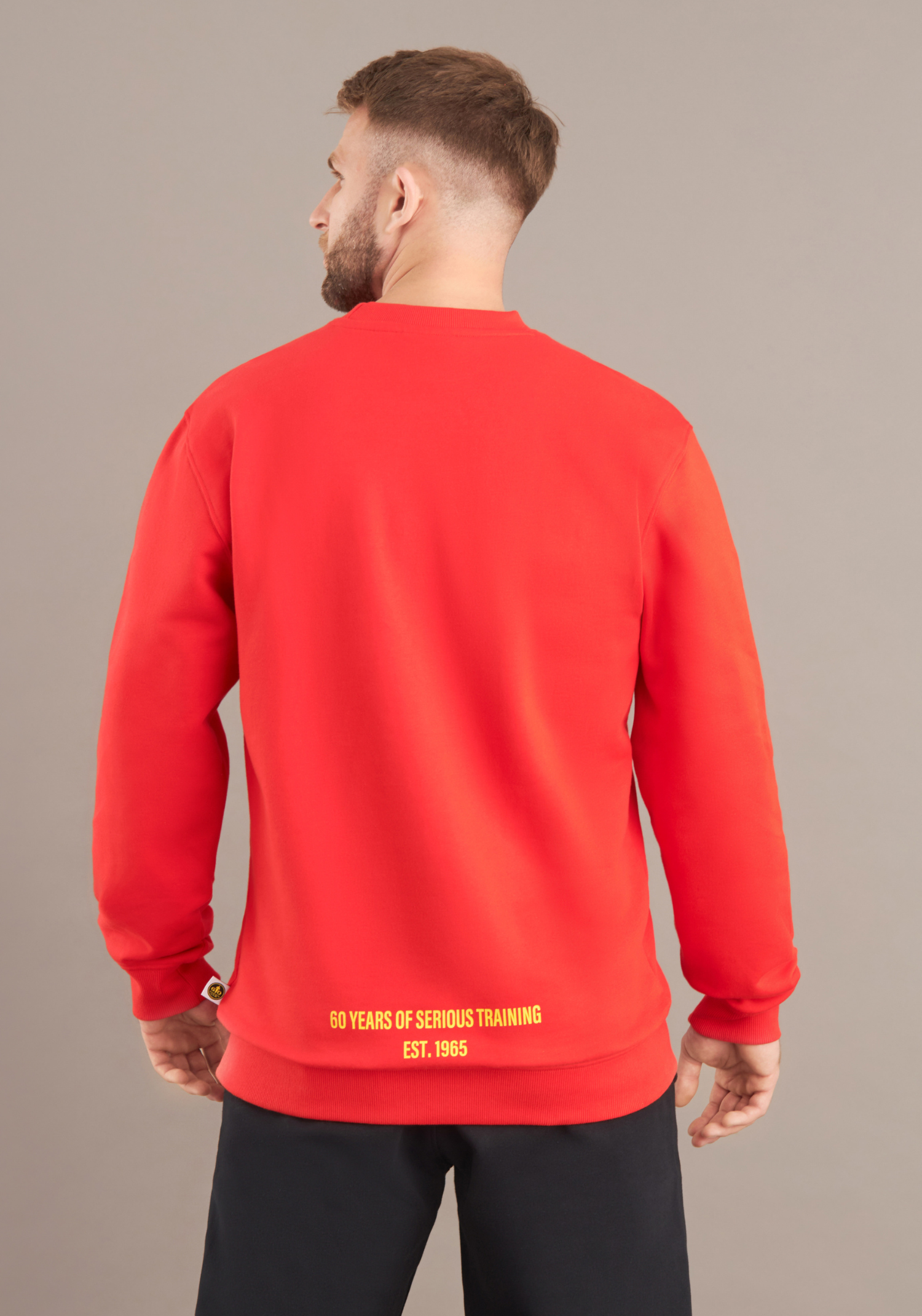 Person wearing a red sweatshirt with yellow text on the back against a beige background
