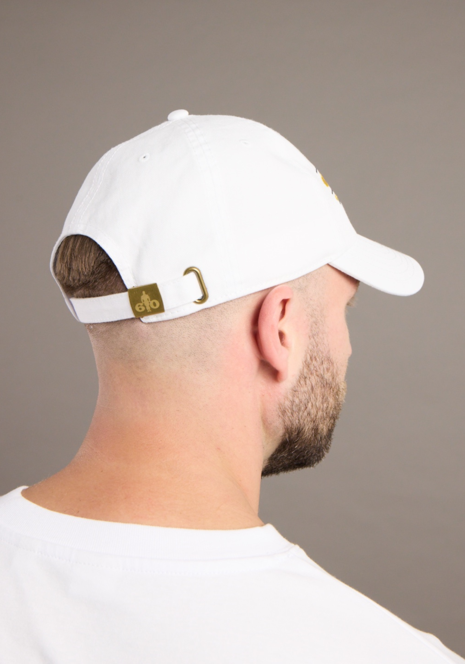 Person wearing a white cap with a gold logo on a plain background