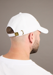 Person wearing a white cap with a gold logo on a plain background