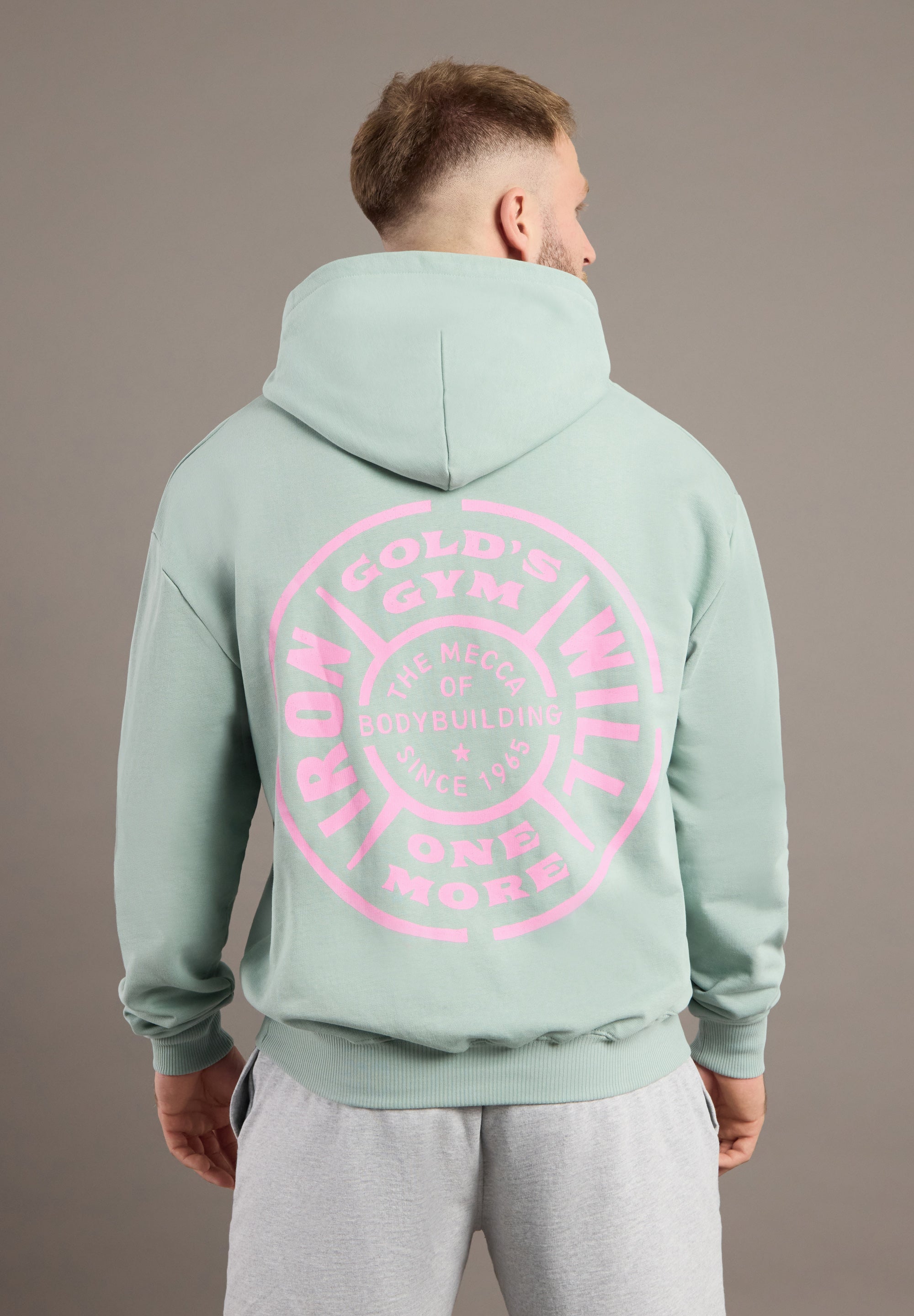 Person wearing a light green hoodie with pink text on the back against a gray background