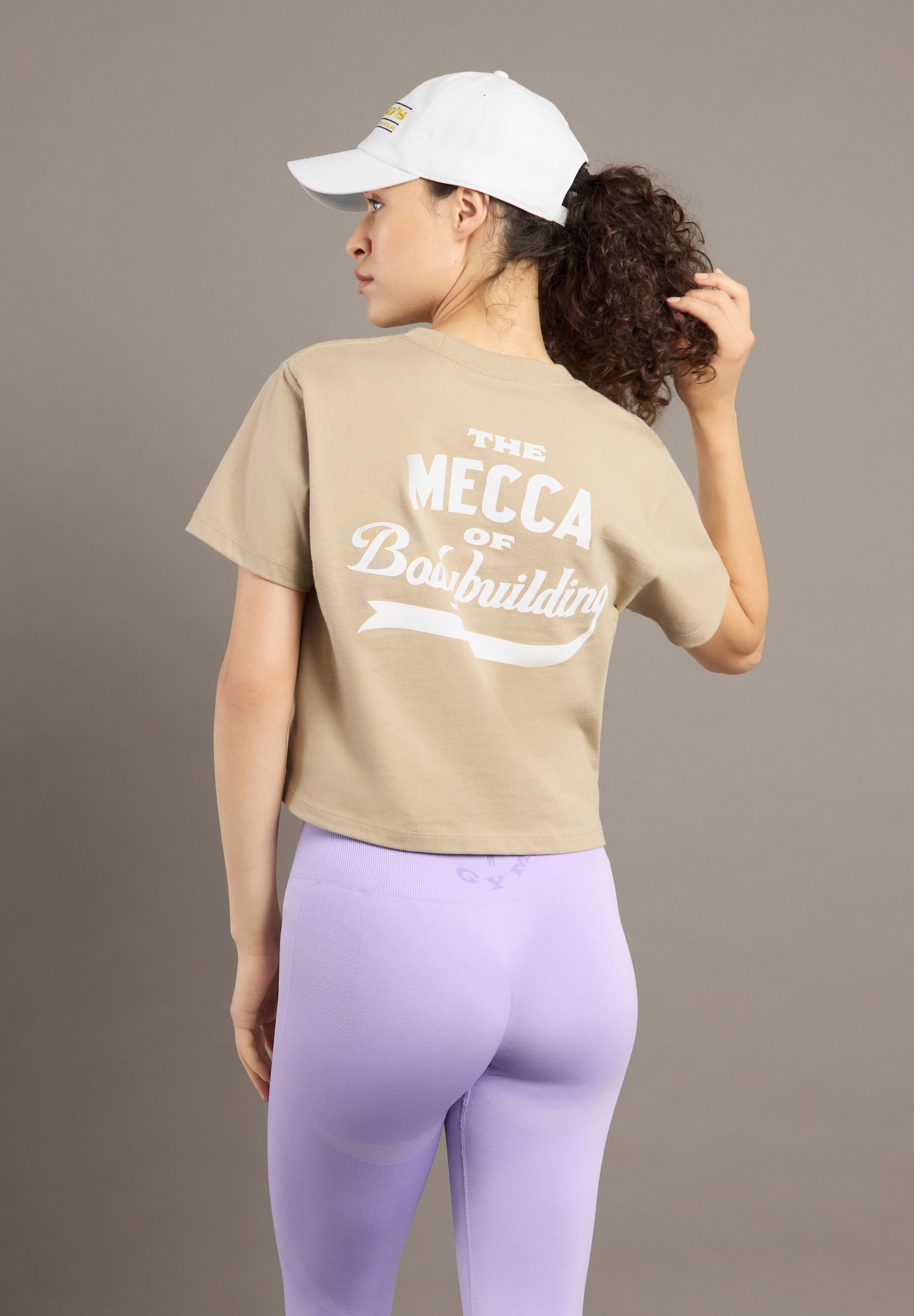 Person wearing a beige t-shirt with text and purple leggings on a plain background