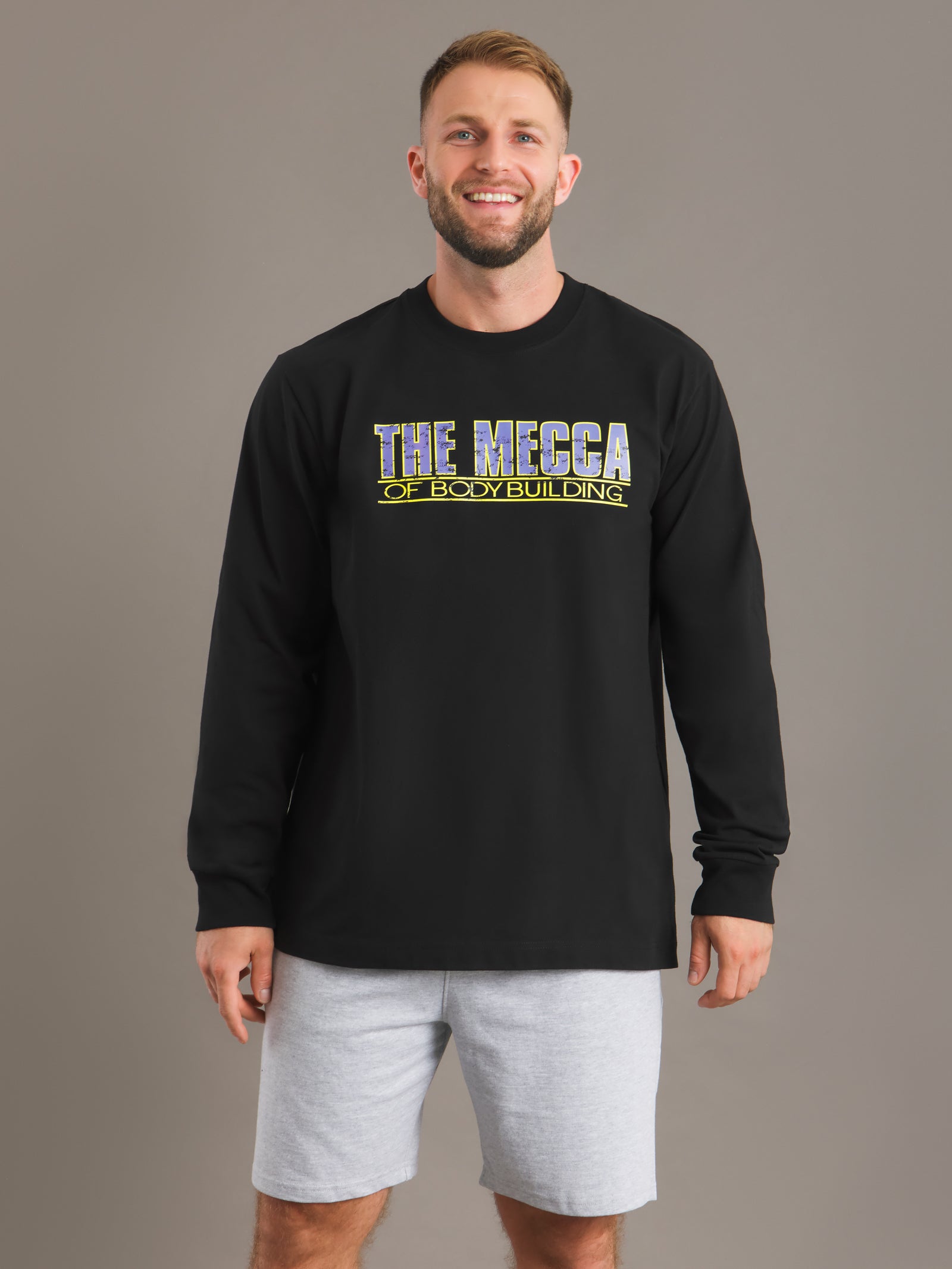 Man wearing a black long-sleeve shirt with 'The Mecca of Bodybuilding' text on a gray background
