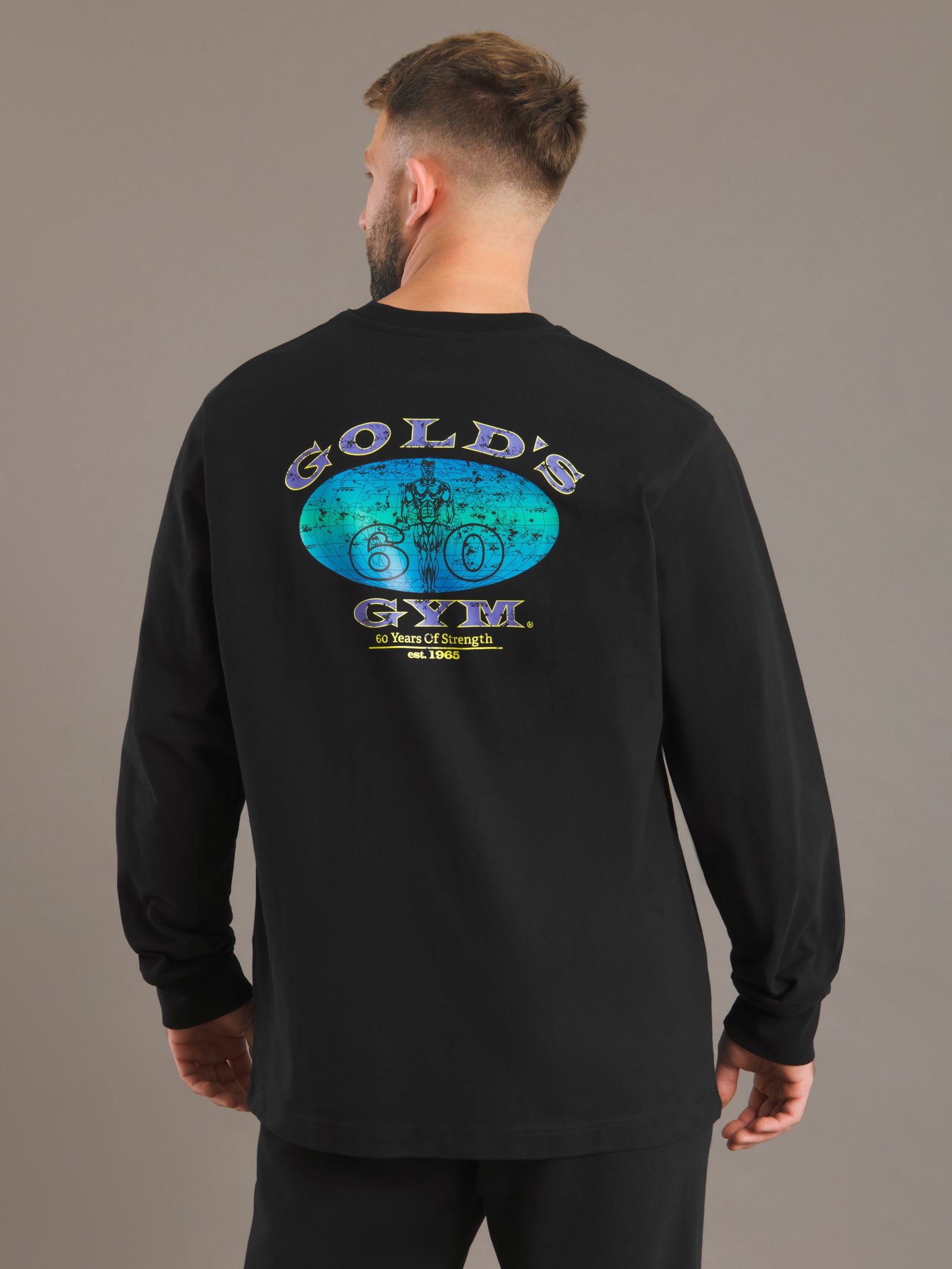 Person wearing a black Gold's Gym sweatshirt with logo on the back against a gray background
