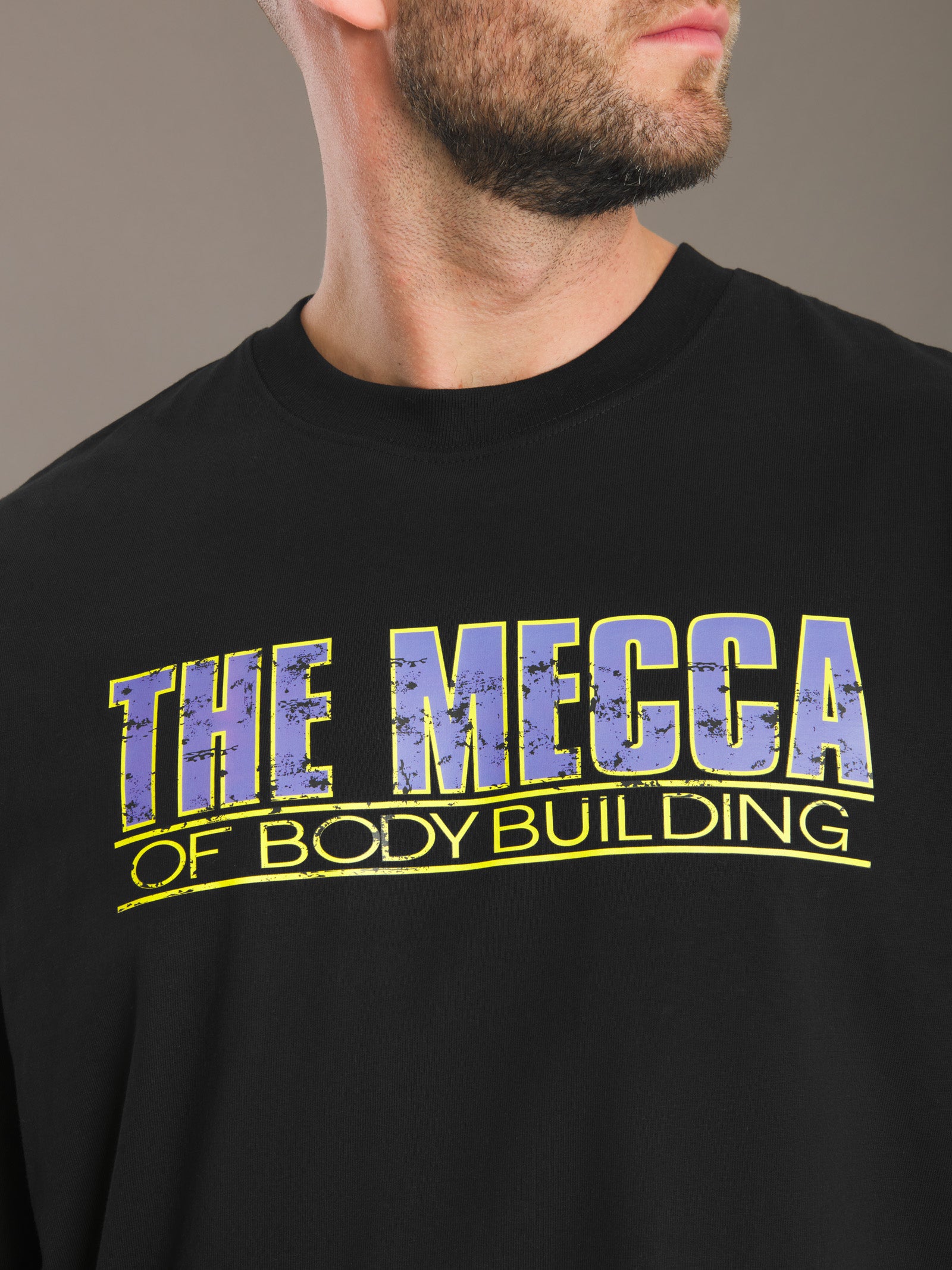 Black t-shirt with 'The Mecca of Bodybuilding' text in yellow and blue on a brown background