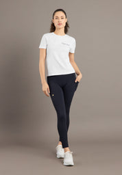 Woman wearing a white t-shirt and black leggings on a brown background