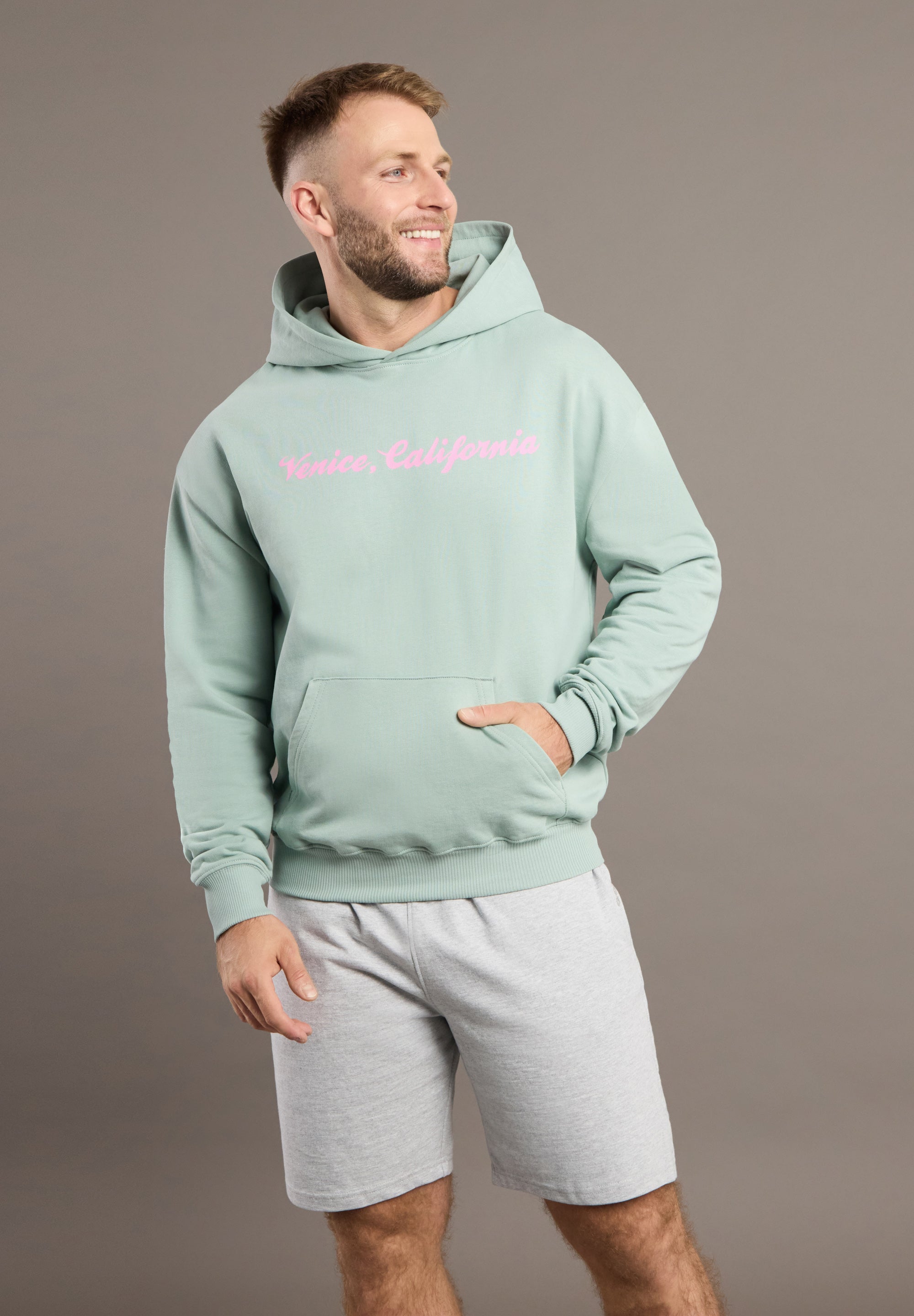 Man wearing a light green hoodie and gray shorts on a brown background