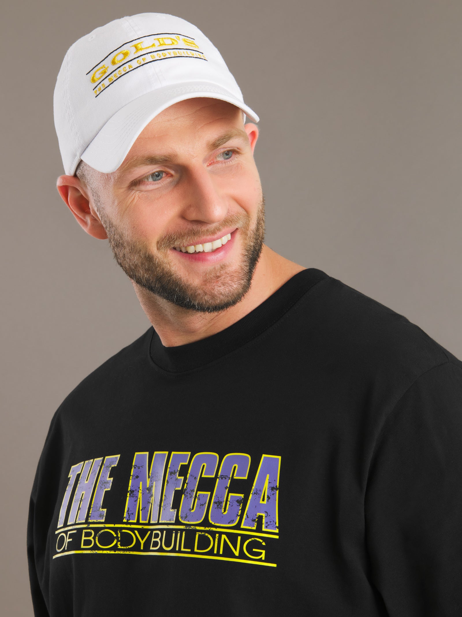 Man wearing a black sweatshirt with 'The Mecca of Bodybuilding' text and a white cap.
