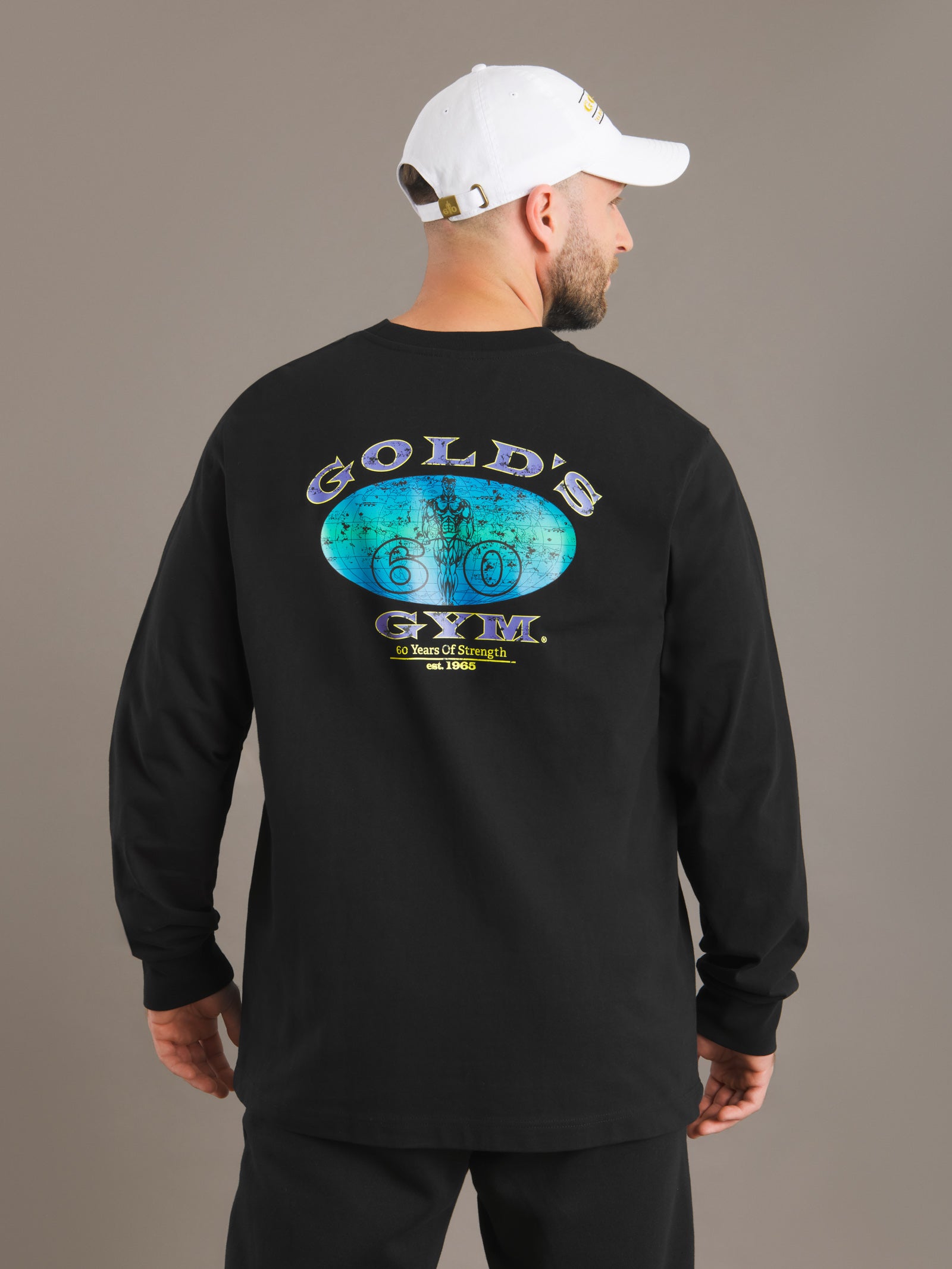 Man wearing a black Gold's Gym long-sleeve shirt with a logo on the back against a gray background