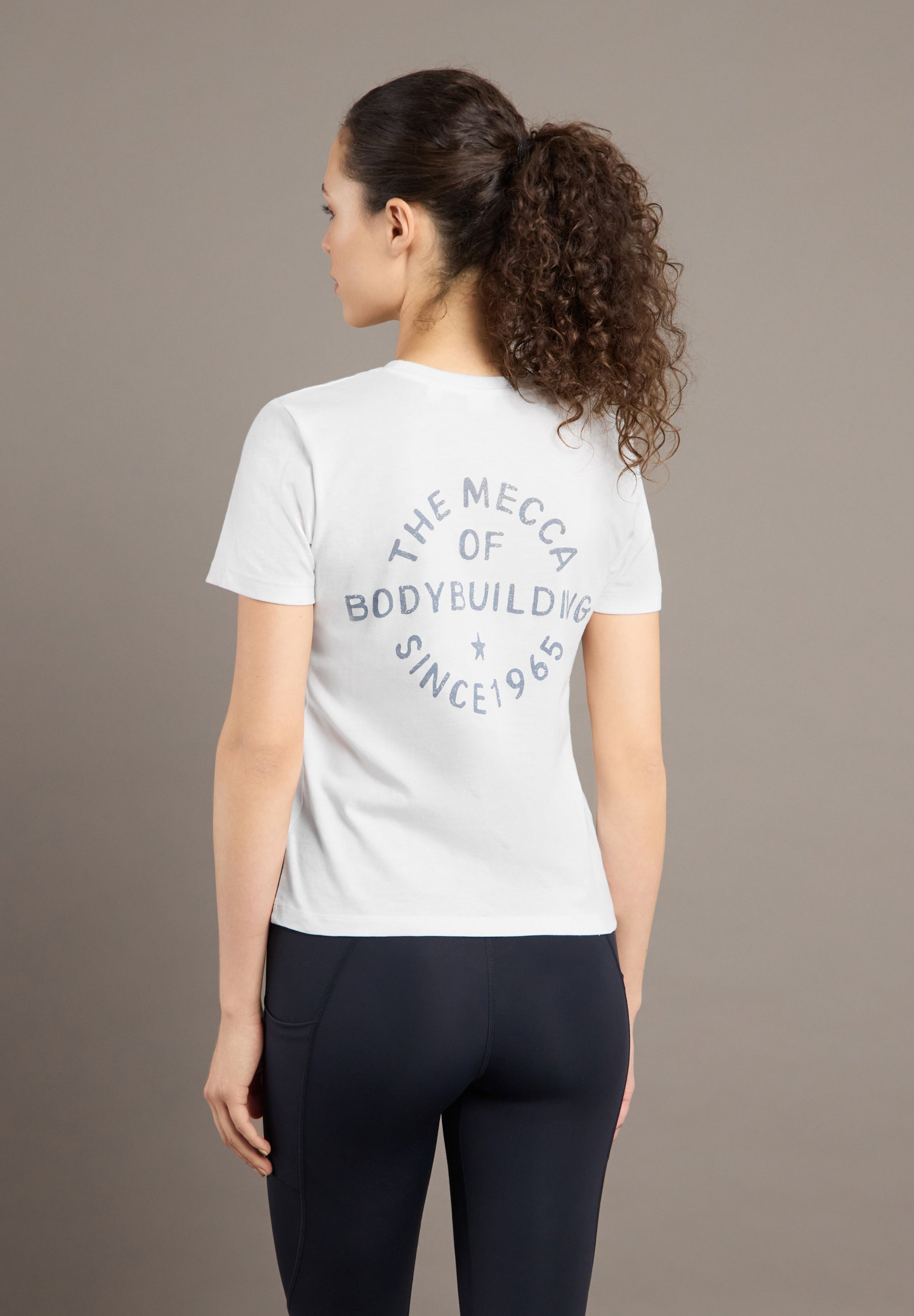 Woman wearing a white t-shirt with text on the back against a brown background