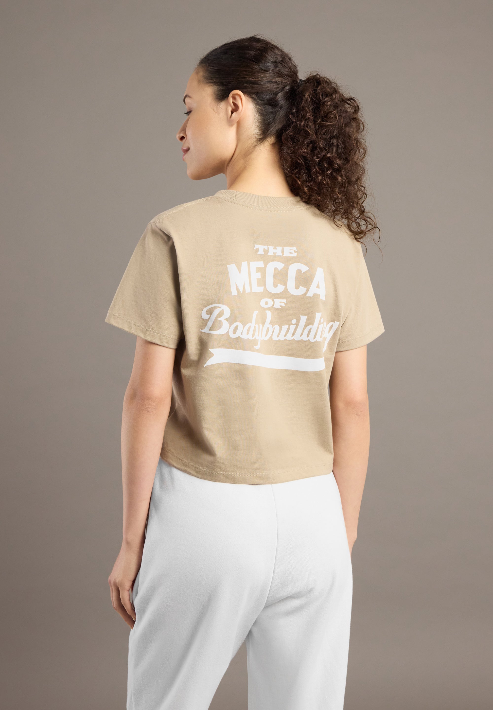 Woman wearing a beige t-shirt with text on the back against a brown background
