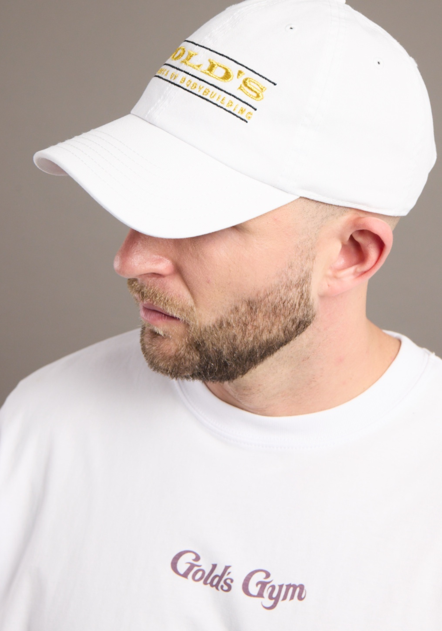 Man wearing a white cap and t-shirt with 'Gold's Gym' branding against a neutral background