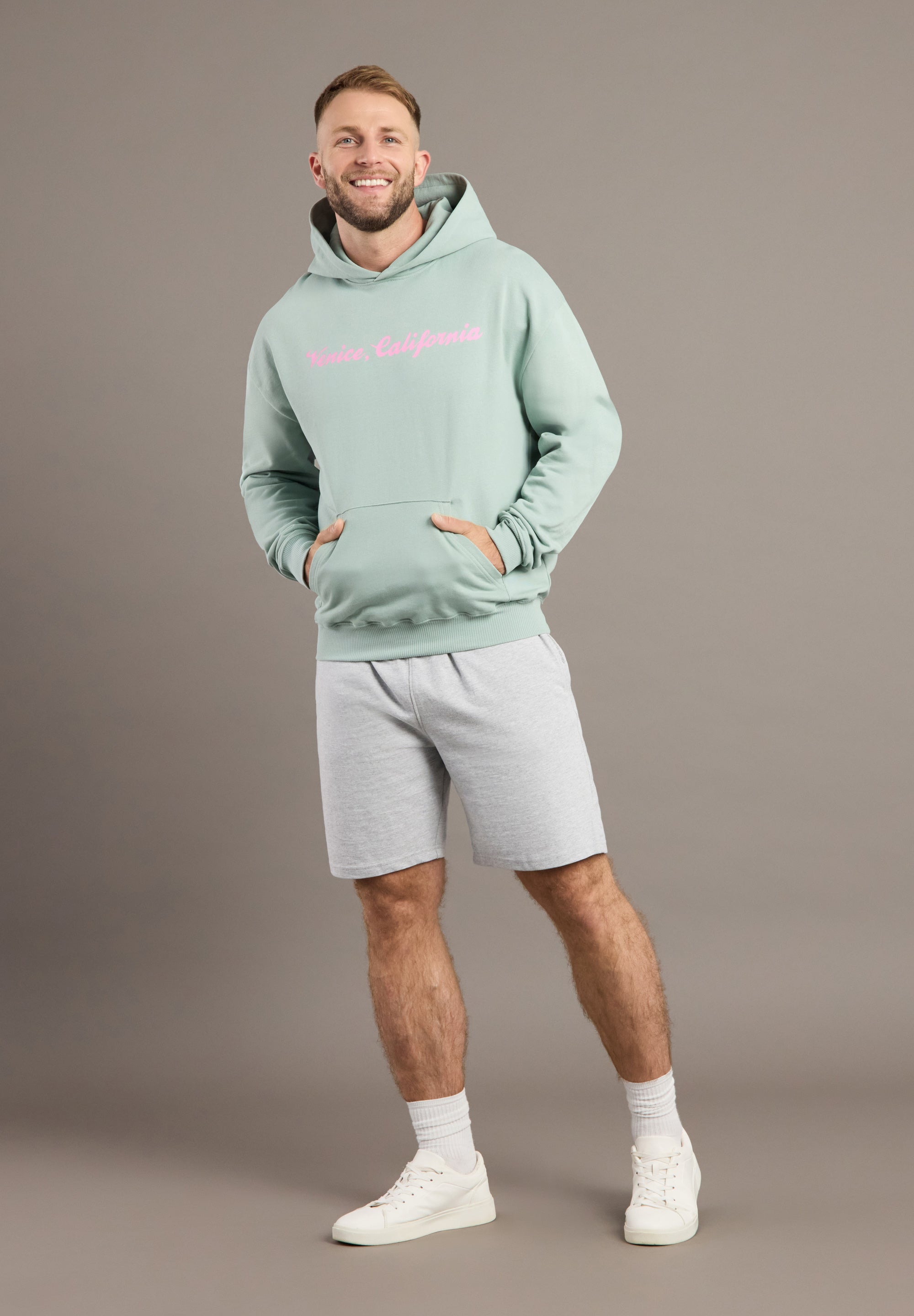 Man wearing a light green hoodie and gray shorts on a brown background