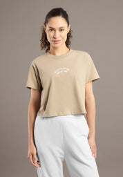 Woman wearing a beige t-shirt with a logo on a brown background