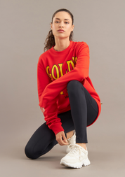 Person wearing a red sweatshirt with yellow text, black pants, and white sneakers on a beige background