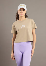 Woman wearing a beige t-shirt and purple leggings with a white cap on a brown background