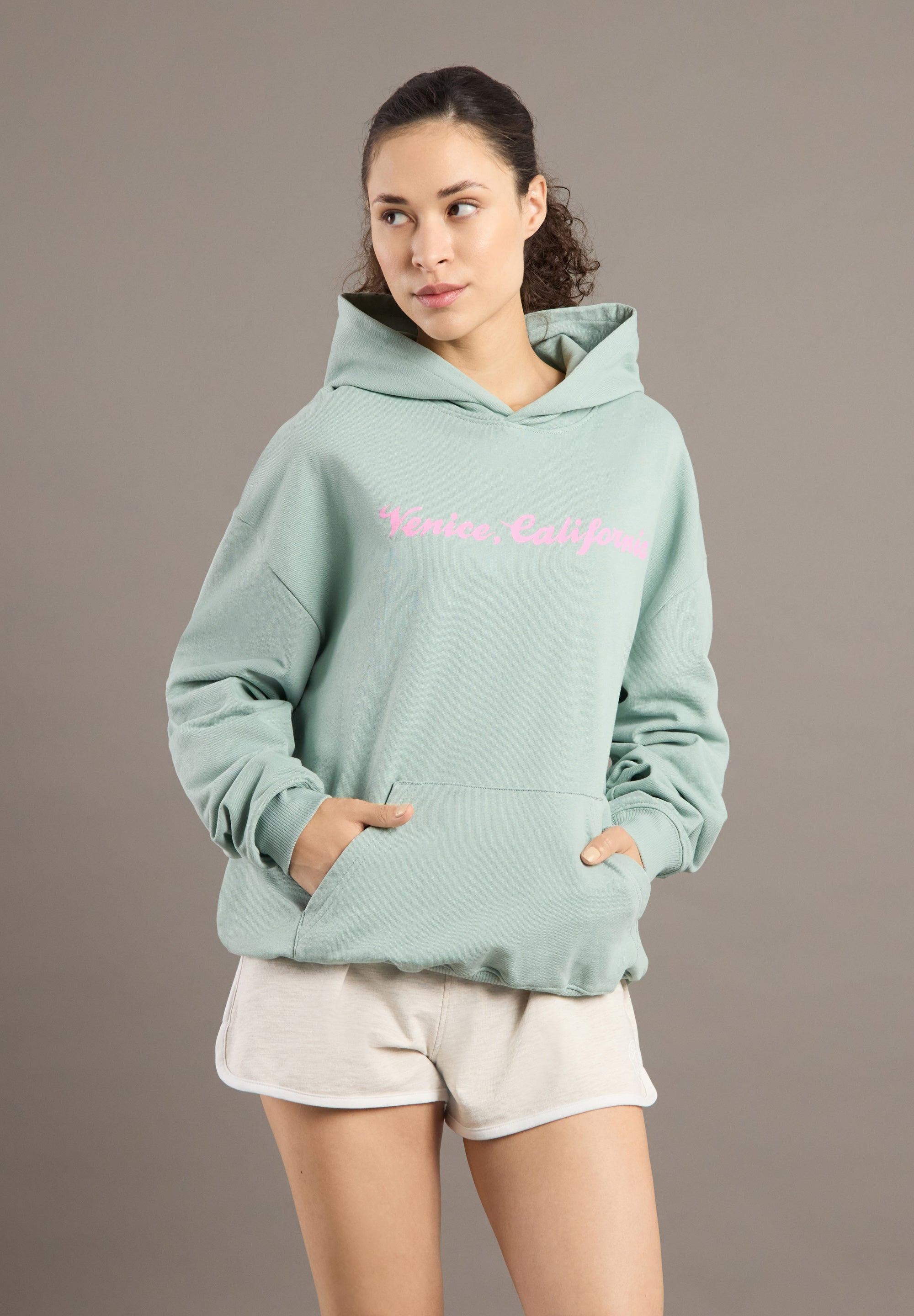Woman wearing a light green hoodie with pink text on a gray background